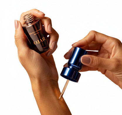 Two hands holding a brown perfume oilbottle and a blue dropper bottle against a beige background