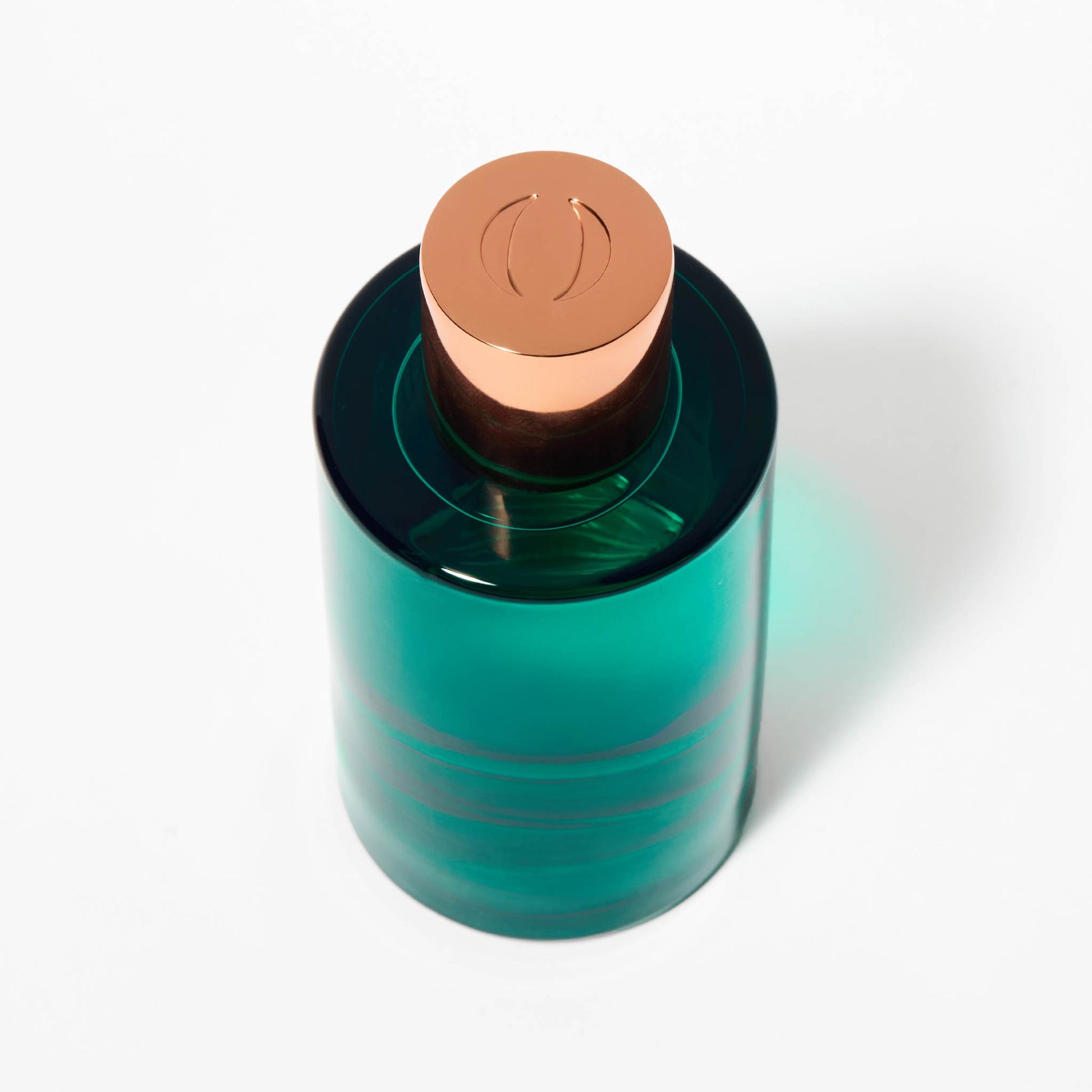 Top view of OJAR perfume bottle in green with letter O engraved on the copper cap on a white background.